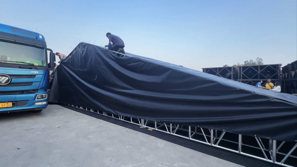 Technicians installing and securing side PVC fabric on aluminum roof truss structure during ongoing event tent construction