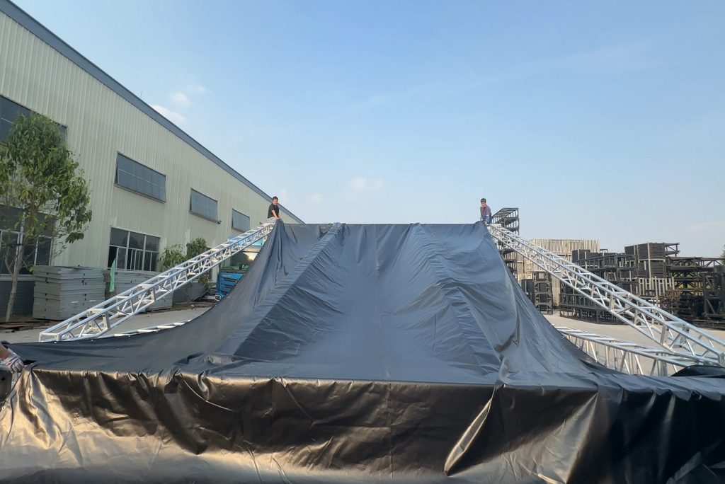 Two technicians working on top of an aluminum roof truss structure during PVC roof fabric installation for outdoor event setup