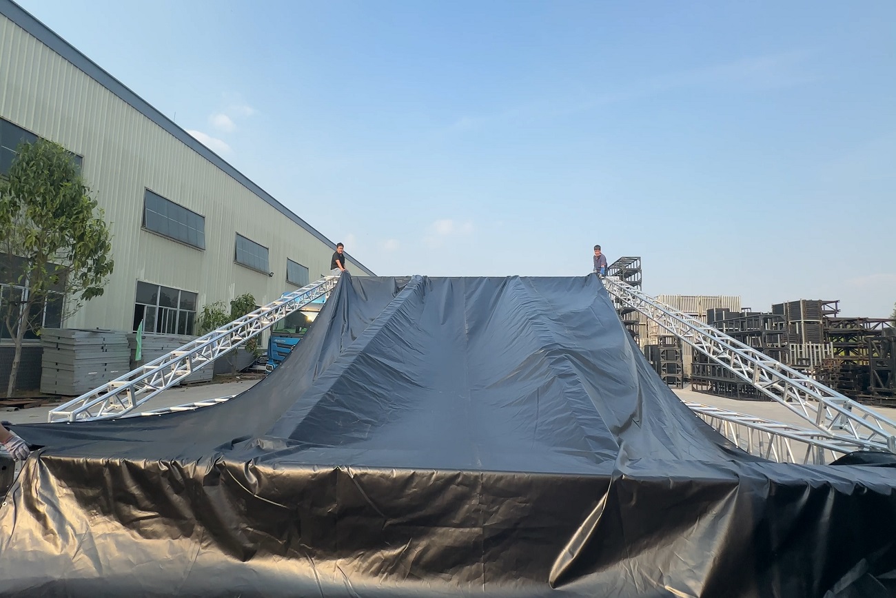 Two technicians working on top of an aluminum roof truss structure during PVC roof fabric installation for outdoor event setup