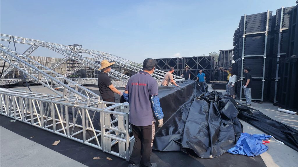 Four workers evenly pulling 450g black PVC roof fabric across an aluminum roof truss structure during installation