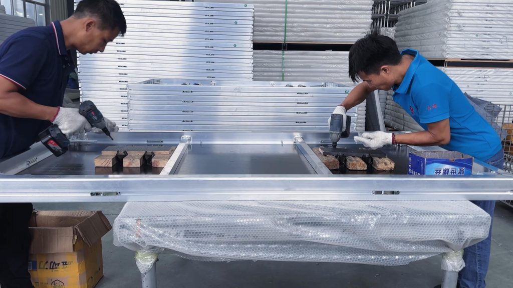Factory workers using electric screwdrivers to fix accessories on a modular stage board before packing