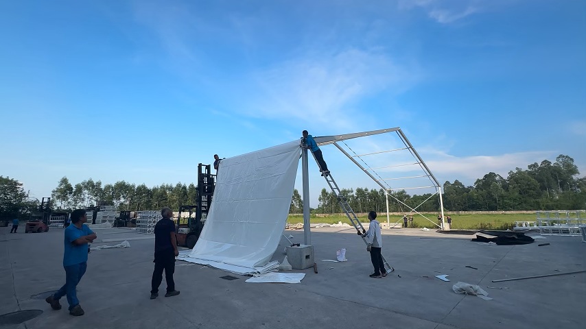 PVC roof cover being positioned on an outdoor event tent frame